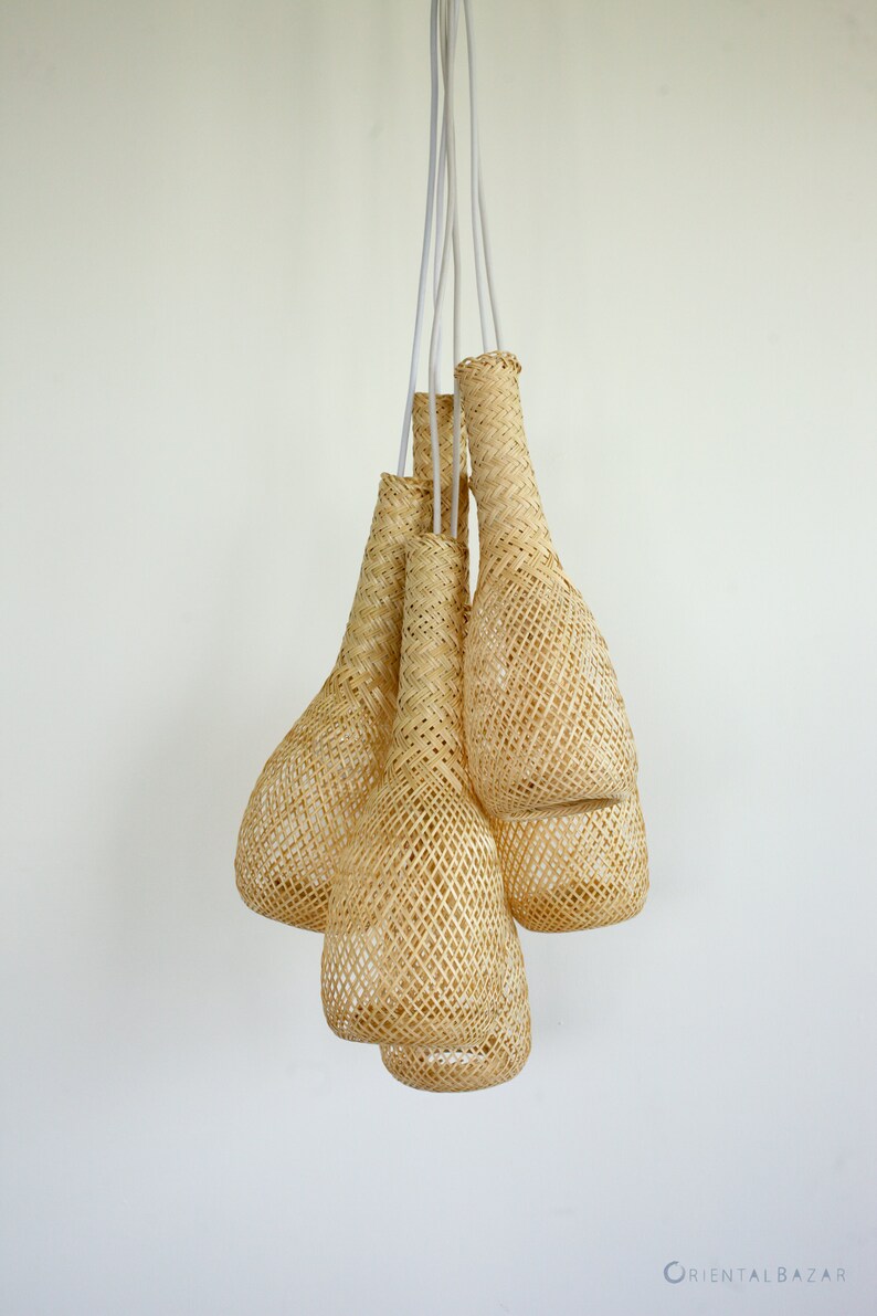 May include: A set of five woven pendant lights, each shaped like a teardrop, hanging from white cords against a white wall. The lights are made of natural woven material, giving them a rustic and organic look.