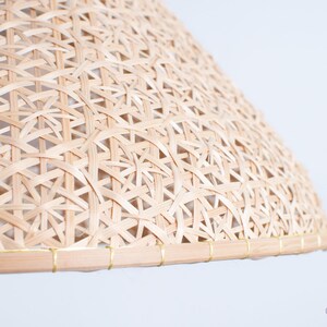 May include: A natural woven lampshade made of light brown bamboo with a gold trim around the edge.
