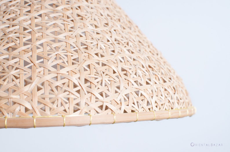 May include: A natural woven lampshade made of light brown bamboo with a gold trim around the edge.
