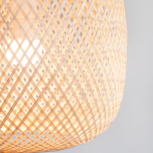 Op de afbeelding: Een close-up van een geweven, lichtbruine, ronde lampenkap gemaakt van natuurlijke materialen. De lampenkap is gemaakt van een kruislings patroon van geweven stroken.