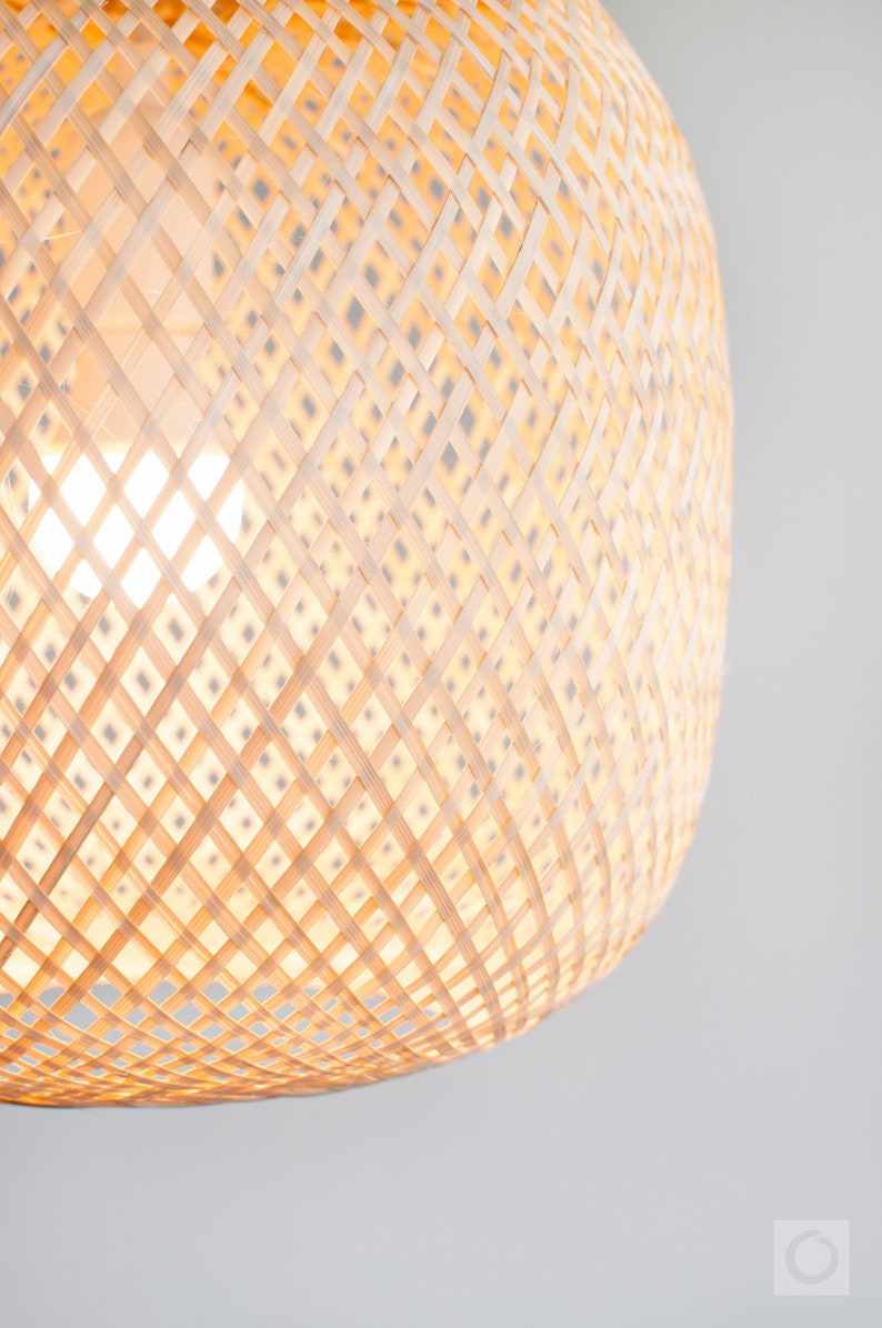 Op de afbeelding: Een close-up van een geweven, lichtbruine, ronde lampenkap gemaakt van natuurlijke materialen. De lampenkap is gemaakt van een kruislings patroon van geweven stroken.