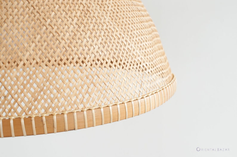May include: Close-up of a natural woven lampshade with a light brown color. The lampshade is made of a woven material with a natural finish. The lampshade has a round shape and a slightly curved top.