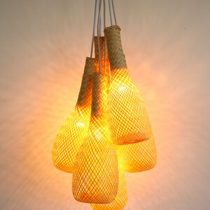 May include: A set of five woven pendant lights, each shaped like a teardrop, hang from a white cord. The lights are made of a natural, light brown material and are illuminated with warm, yellow light.