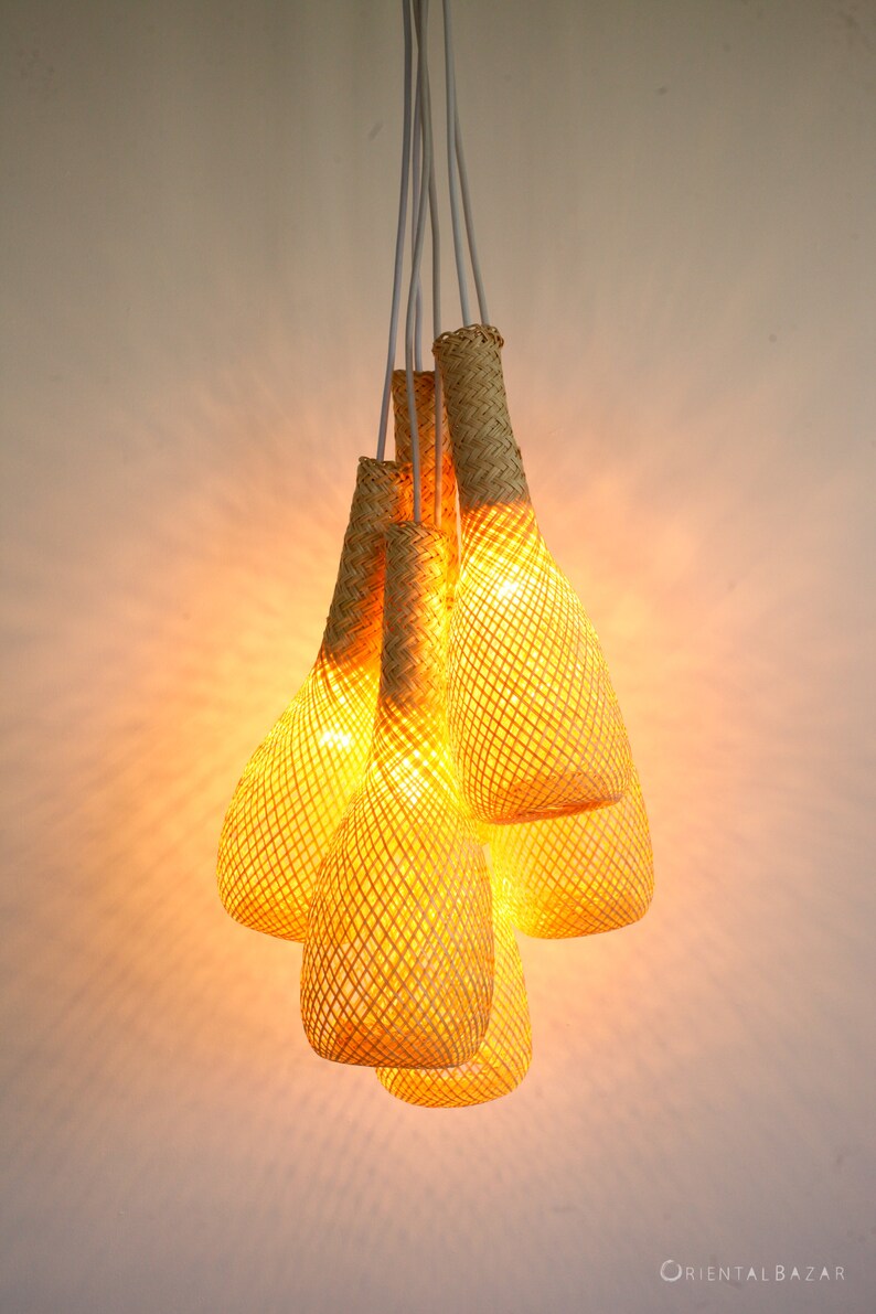 May include: A set of five woven pendant lights, each shaped like a teardrop, hang from a white cord. The lights are made of a natural, light brown material and are illuminated with warm, yellow light.