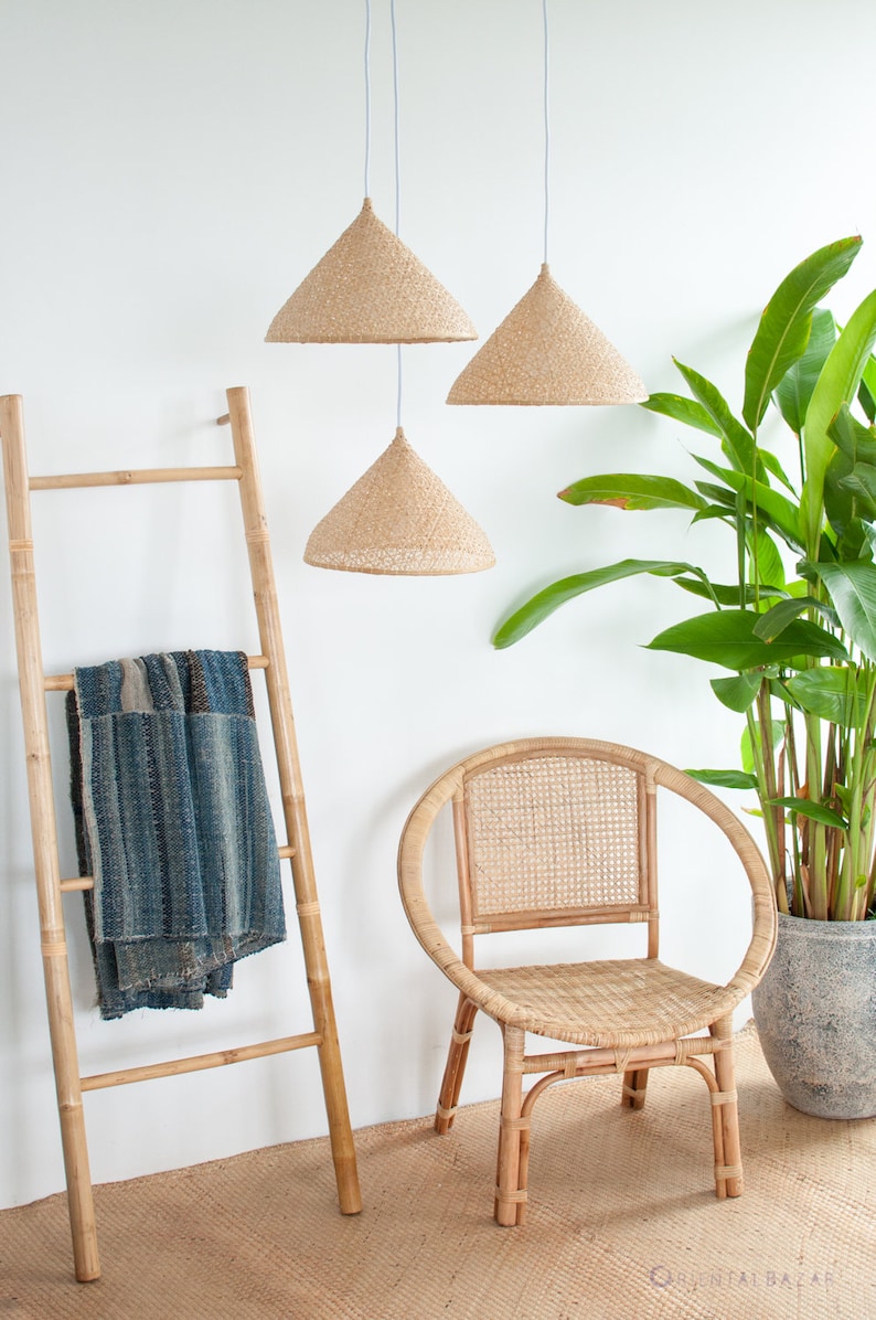 May include: Three woven pendant lights hang from the ceiling above a bamboo ladder with a blue and white throw blanket draped over it. A woven rattan chair sits in front of a potted green plant.
