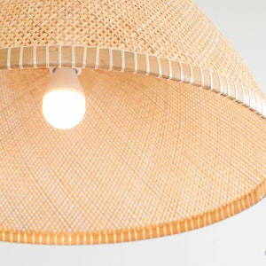May include: A close-up of a woven light fixture with a white light bulb. The fixture is made of natural materials and has a light brown color.
