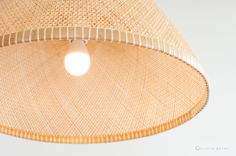 May include: A close-up of a woven light fixture with a white light bulb. The fixture is made of natural materials and has a light brown color.