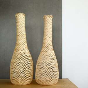 May include: Two woven wicker vases with a diamond pattern, sitting on a wooden table.