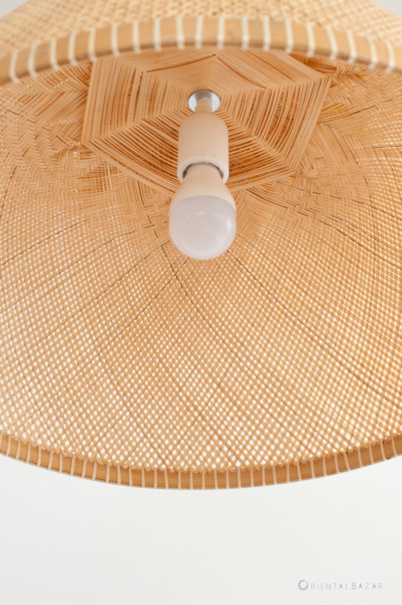 May include: A close-up of a woven wicker lampshade with a white light bulb inside. The lampshade is made of natural materials and has a light brown color.