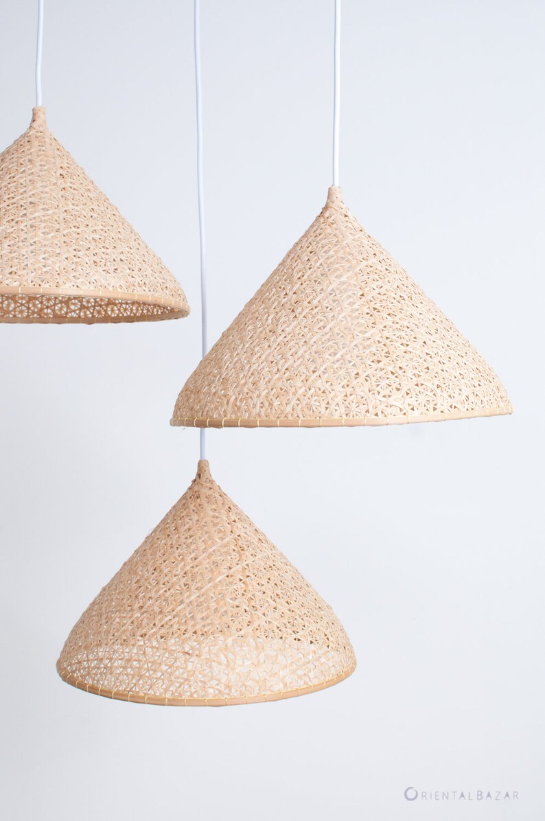 May include: Three woven, cone-shaped pendant lights hang from white cords against a white background. The lights are made of natural, light brown material and have a delicate, intricate pattern.