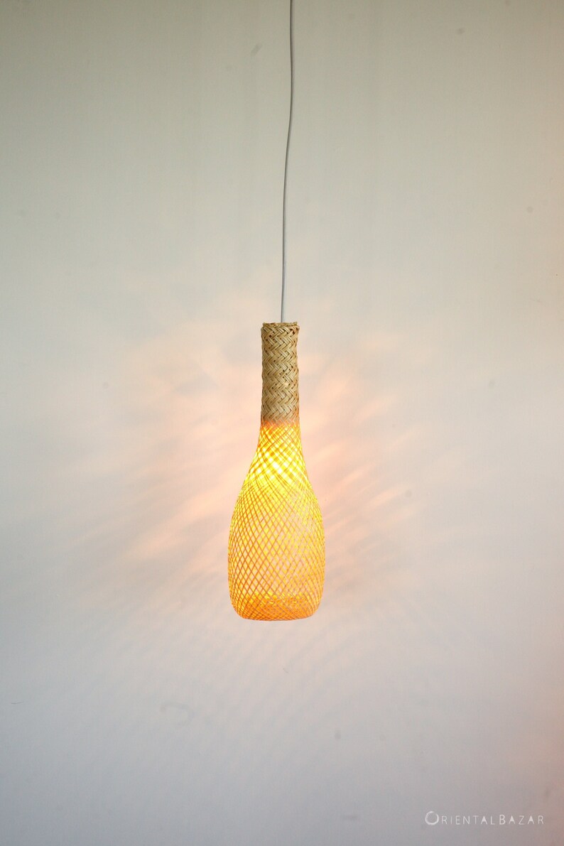 May include: A woven, light brown, bottle-shaped pendant light fixture hangs from a white ceiling. The light is on, casting a warm glow through the woven material.