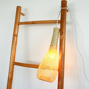May include: A woven rattan pendant light hangs from a wooden ladder. The light is turned on and emits a warm glow.