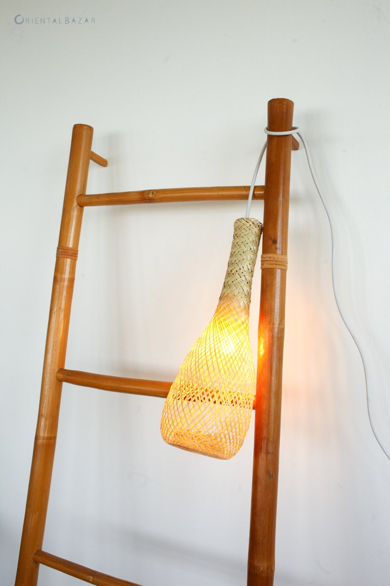May include: A woven rattan pendant light hangs from a wooden ladder. The light is turned on and emits a warm glow.