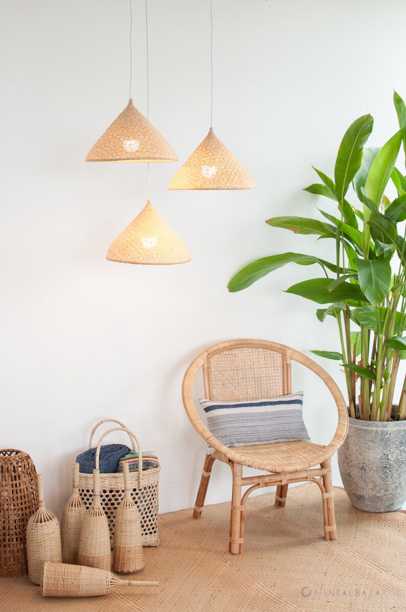 May include: Three woven conical pendant lights hang from the ceiling in a white room. A wicker chair with a striped cushion sits in the corner, next to a potted plant. Several woven baskets are on the floor.