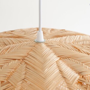 May include: Close-up of a woven, natural-toned, round pendant light fixture. The light fixture is made of woven bamboo or rattan and has a white cord.