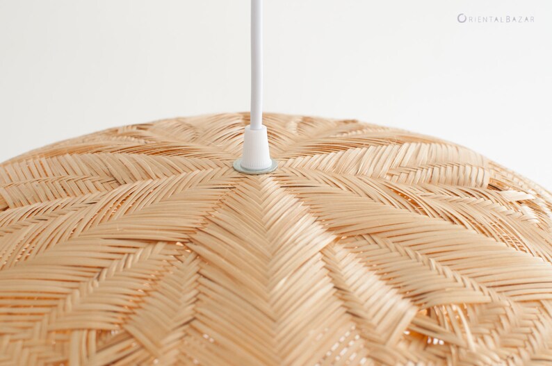 May include: Close-up of a woven, natural-toned, round pendant light fixture. The light fixture is made of woven bamboo or rattan and has a white cord.