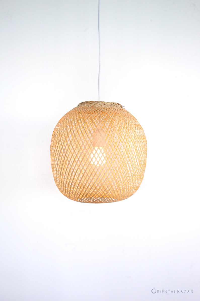 Op de afbeelding: Een ronde, natuurlijke geweven bamboe hanglamp met een wit snoer.