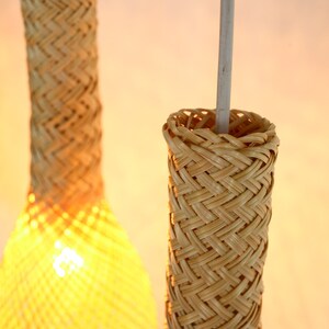 May include: Two woven bamboo pendant lights with a natural beige color. The lights are hanging from a white cord.