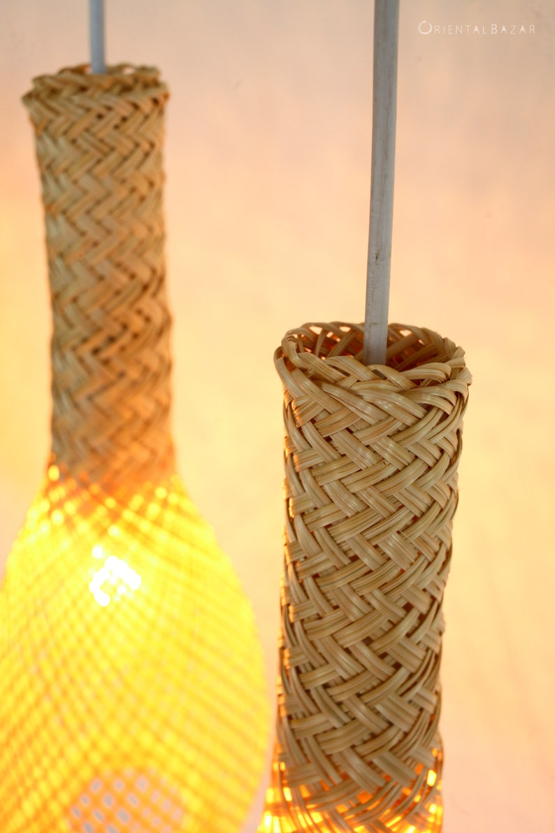 May include: Two woven bamboo pendant lights with a natural beige color. The lights are hanging from a white cord.