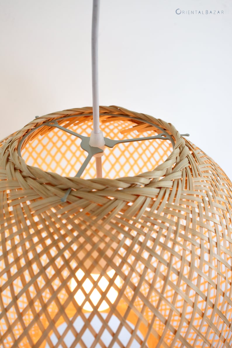 Op de afbeelding: Een geweven bamboe hanglamp met een wit snoer. De lamp is rond en heeft een geweven patroon.