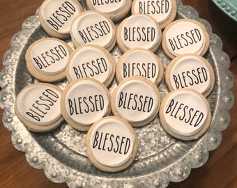 May include: A silver tray with 13 round cookies decorated with white icing and the word "Blessed" in black lettering.