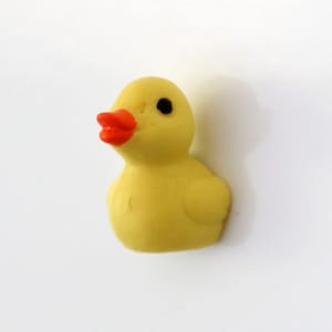 Könnte beinhalten: Eine kleine gelbe Gummiente mit einem leuchtend orangefarbenen Schnabel und schwarzen Augen. Die Ente ist ein klassisches Spielzeug, das oft in Badewannen oder als Dekorationsartikel verwendet wird. Die Ente hat ein fröhliches und verspieltes Design.
