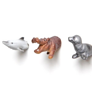 Könnte beinhalten: Drei kleine Tierfiguren, ein grauer Delfin, ein braunes Flusspferd mit offenem Maul und eine silberne Robbe. Die Figuren sind alle nach rechts ausgerichtet.
