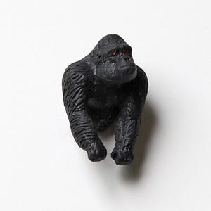 Op de afbeelding: Een kleine, zwarte gorilla figuur met rode ogen. De gorilla staat in een loop houding, met zijn armen en benen uitgestrekt. Het beeldje is gemaakt van een stevig materiaal en heeft een getextureerd oppervlak. De achtergrond is effen wit.