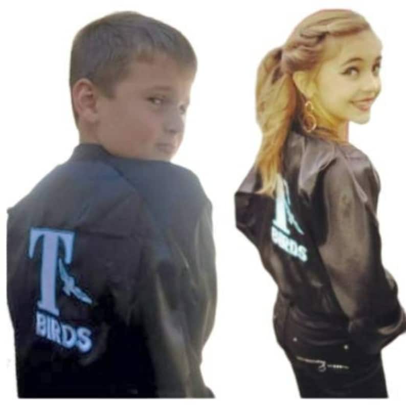 Puede incluir: Dos ni&ntilde;os con chaquetas de sat&eacute;n negro con un logotipo blanco de "T Birds" en la espalda. La chaqueta del ni&ntilde;o tiene un gr&aacute;fico de p&aacute;jaro azul en el lado izquierdo del pecho.