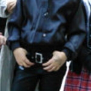 Puede incluir: Una persona joven con una camisa negra de botones, cintur&oacute;n negro y pantalones vaqueros azul oscuro. Est&aacute; de pie con las manos en las caderas.