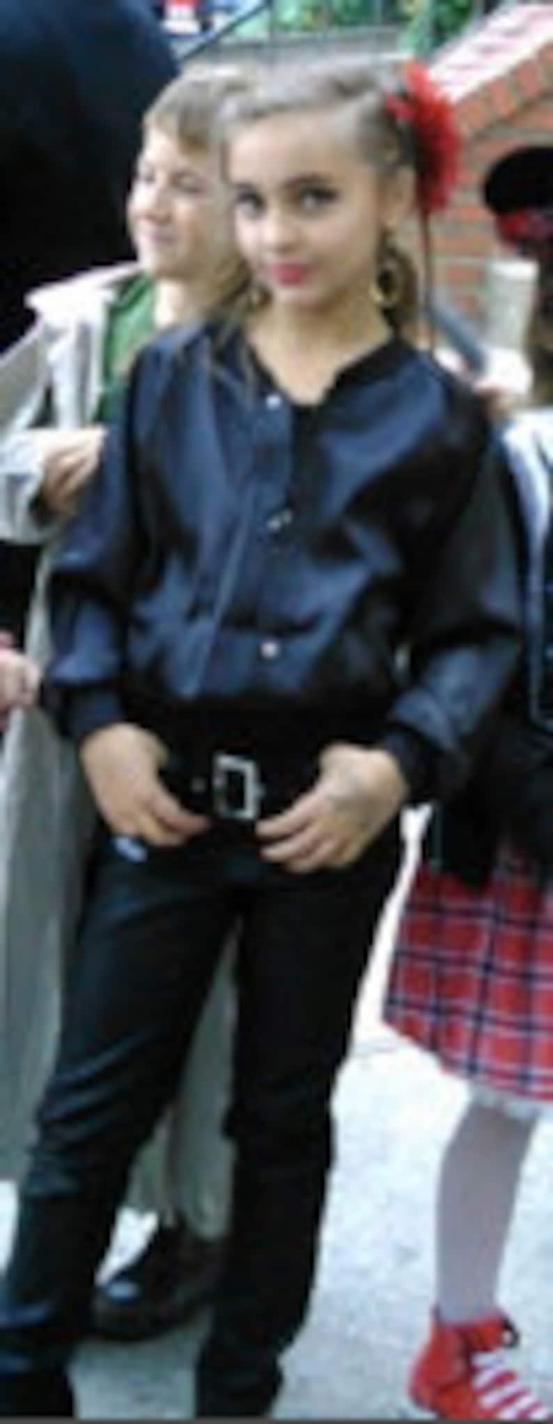 Puede incluir: Una persona joven con una camisa negra de botones, cintur&oacute;n negro y pantalones vaqueros azul oscuro. Est&aacute; de pie con las manos en las caderas.