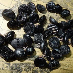Peut inclure: Une collection de boutons en verre noir avec différents motifs et designs. Les boutons sont de tailles et de formes différentes, et certains ont une finition brillante.