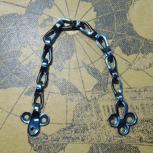 May include: A black metal chain with two decorative clasps. The chain is made of oval links and the clasps have a clover-like design.