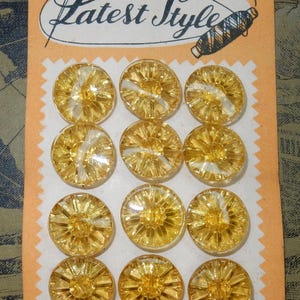 Può includere: Una scheda di dodici bottoni vintage gialli trasparenti. Ogni bottone ha un design a forma di stella. La scheda riporta la scritta "Latest Style". È presente anche una bobina di filo.