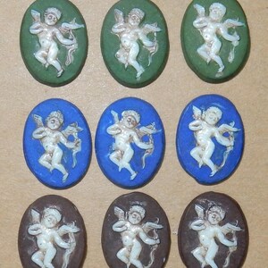 Può includere: Nove pendenti a cammeo ovali raffiguranti un cherubino bianco con arco e freccia. I cammei sono ambientati su sfondi verdi, blu e marroni. I cherubini sono in rilievo, creando un effetto tridimensionale.