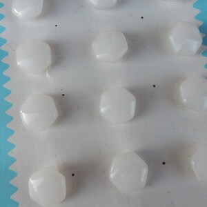 May include: A sheet of white card with 12 white, hexagonal buttons attached. The buttons are arranged in rows and columns.
