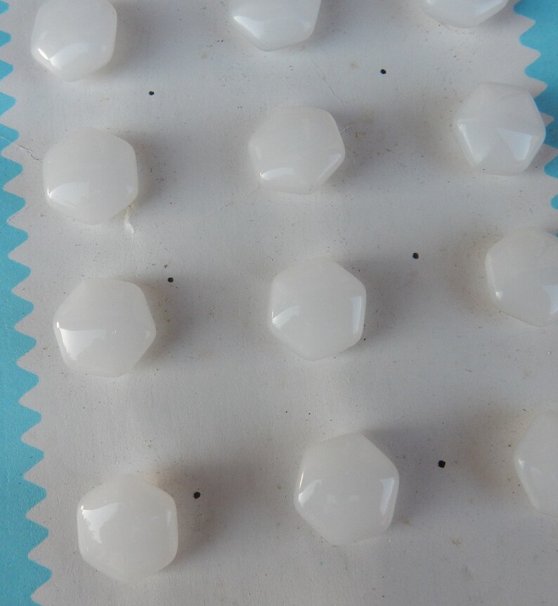 May include: A sheet of white card with 12 white, hexagonal buttons attached. The buttons are arranged in rows and columns.