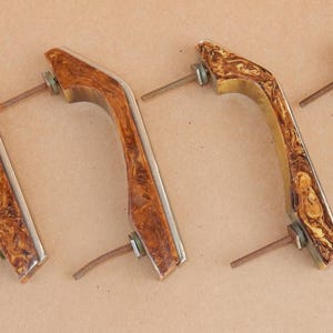 May include: Set of four brown and gold cabinet door pulls with silver screws. The pulls have a wood grain pattern.