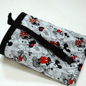May include: A black and white drawstring bag with a Mickey Mouse and Minnie Mouse print. The bag has a black adjustable strap with a buckle.