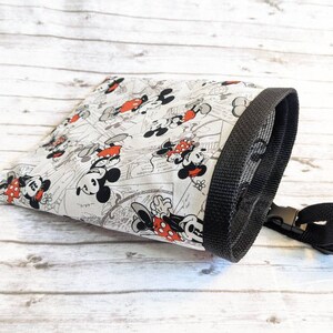 May include: A white drawstring bag with a black trim and a black mesh top. The bag features a repeating pattern of Mickey Mouse and Minnie Mouse in black and red.