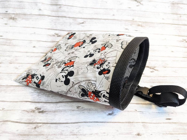 May include: A white drawstring bag with a black trim and a black mesh top. The bag features a repeating pattern of Mickey Mouse and Minnie Mouse in black and red.