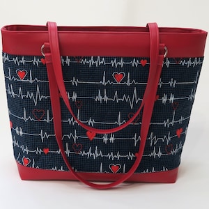 May include: Red tote bag with a blue fabric lining featuring a pattern of white EKG lines and red hearts. The bag has two red straps.