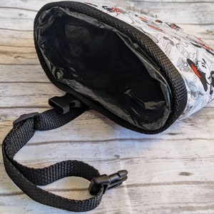 May include: A black and white dog poop bag dispenser with a Mickey Mouse and Minnie Mouse print. The dispenser has a black strap with a buckle.