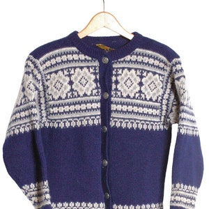 Puede incluir: Un cárdigan azul y blanco de punto con un patrón escandinavo tradicional. El cárdigan tiene un cierre de botones y mangas largas.