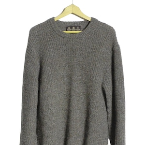May include: A grey, ribbed-knit jumper with a crew neck, suspended from a wooden hanger. The jumper has a textured appearance and a label at the back of the neck. The sleeves have a ribbed cuff. The jumper is made of a thick, warm material.