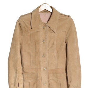 May include: A tan suede jacket with a button-up front and two large pockets. The jacket has a collar and long sleeves.