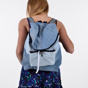 May include: A blue denim backpack with a white drawstring closure. The backpack is worn by a person wearing a floral print skirt.