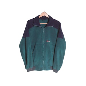 May include: A long-sleeve fleece jacket featuring a colour-blocked design in dark navy blue and forest green. The jacket has a full-length front zip, a high collar, and a small red and white Berghaus logo embroidered on the chest area.