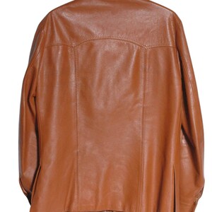 May include: A brown leather jacket hanging on a wooden hanger. The jacket has a classic design with a collar, button closure, and pockets. The leather appears to be smooth and has a slight sheen. The jacket is a medium brown color.