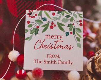 May include: A Christmas gift tag with the words "merry Christmas" and "FROM, The Smith Family" in red script. The tag is decorated with green leaves and red berries. A red and black plaid fabric is in the background, along with pine cones and decorative berries.